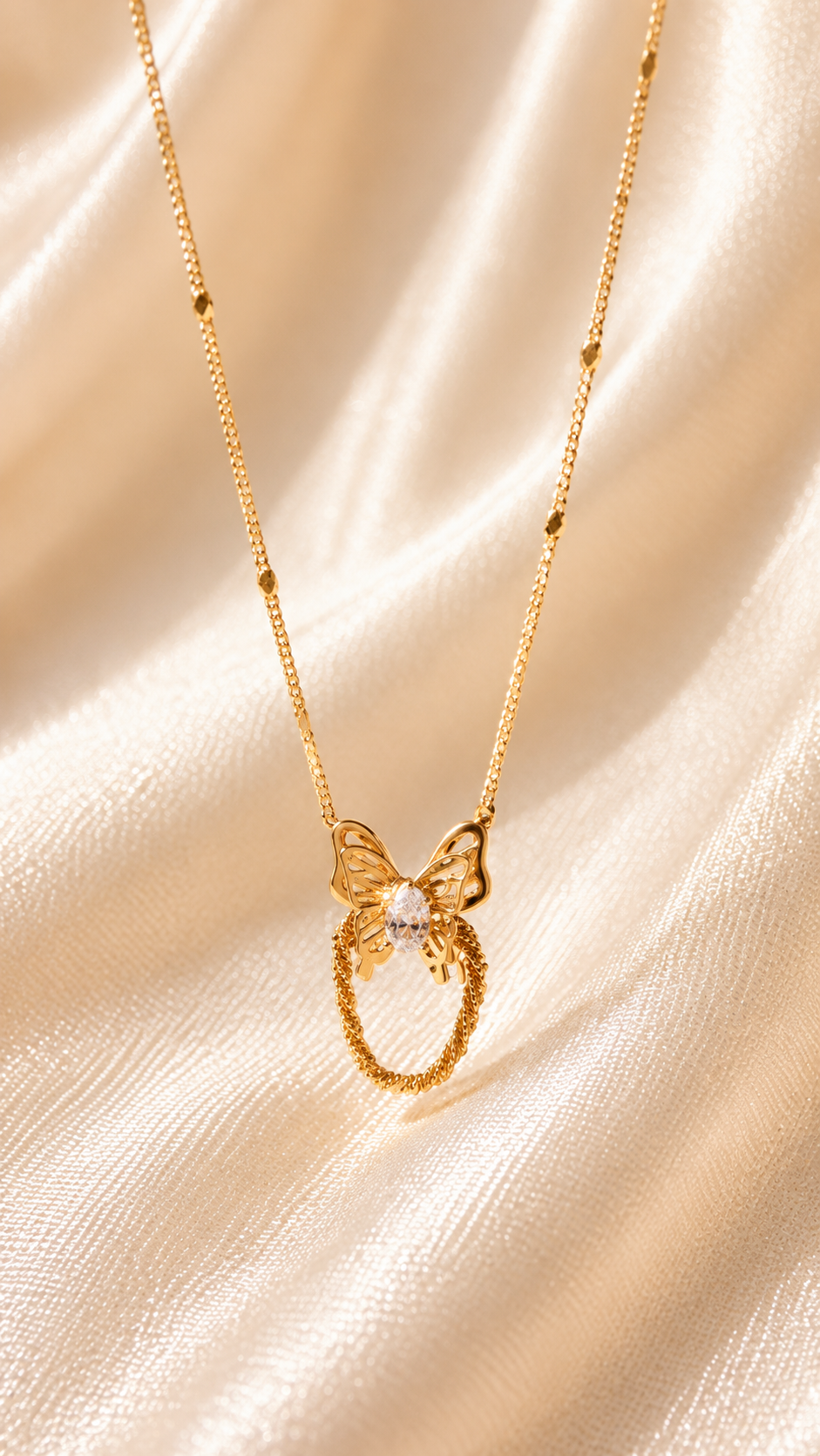 A delicate gold necklace featuring a butterfly pendant with a small clear central stone, hanging from a fine gold chain against a draped champagne satin fabric background.