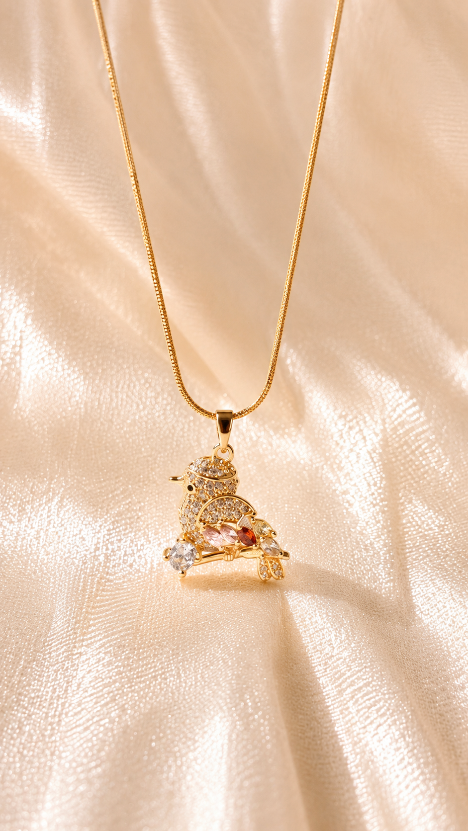 A gold chain necklace with a small decorative pendant featuring a lion and a pink gemstone, displayed on a shimmering cream satin fabric background.